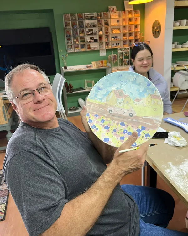 A customer holding up his plate painted with houses, a pink car and flowers
