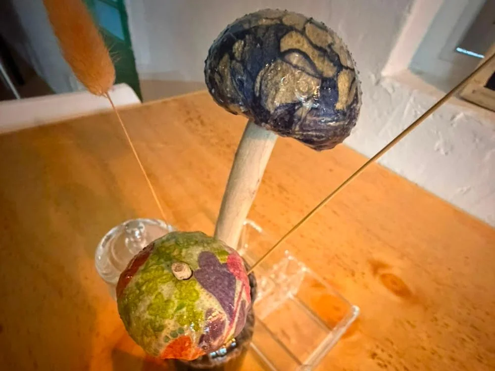 Two of Katy's table flowers: decoupaged and glazed sea shells in blue, gold, green and purple, on wooden stems