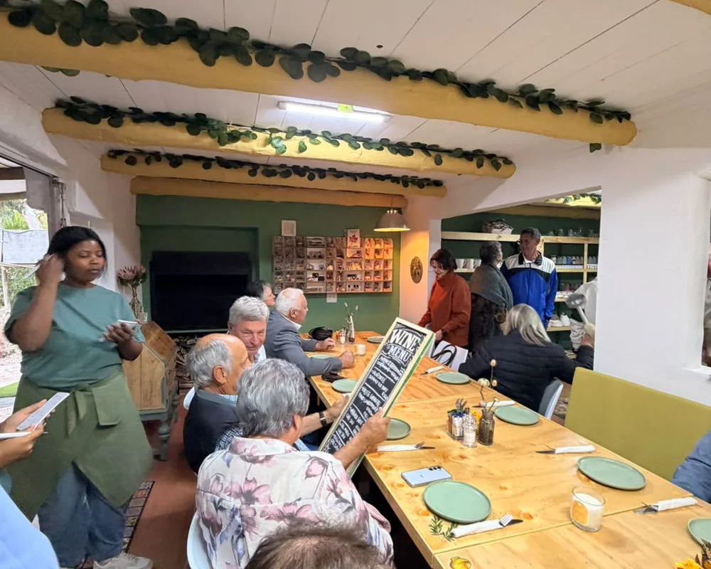 A group seated along the long table for a function, with green plates set out and a wine menu board being passed around
