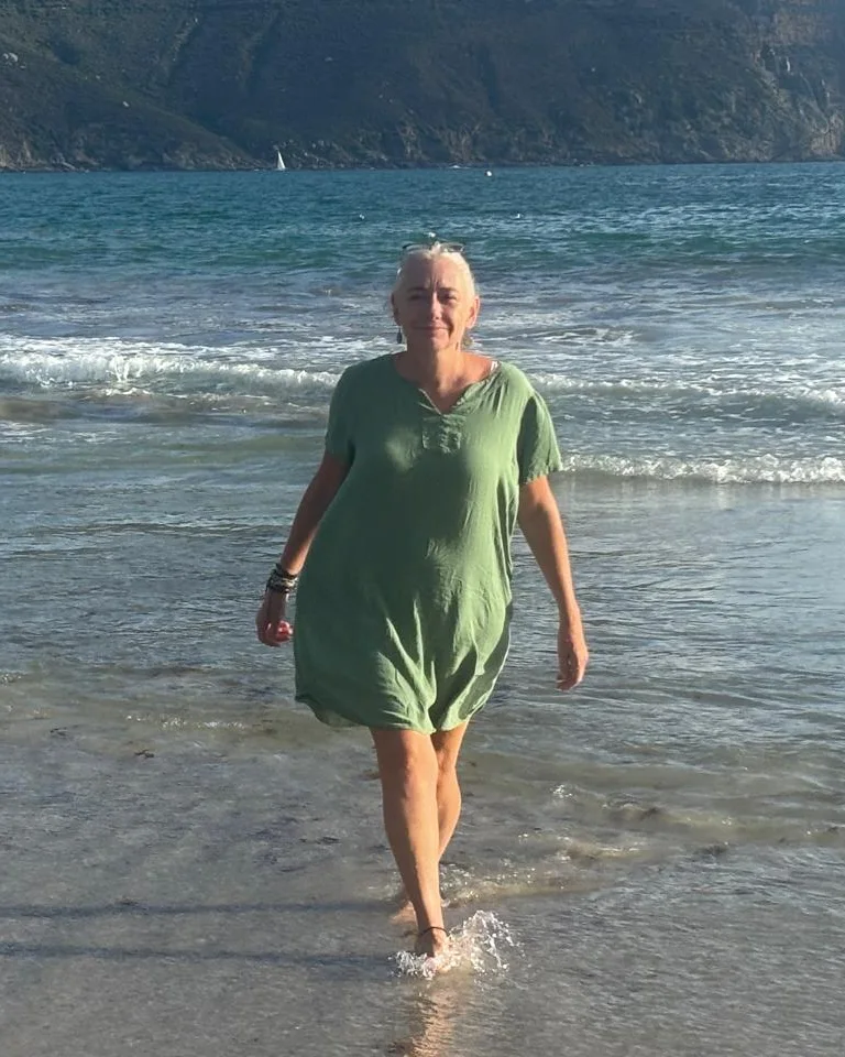 Katy walking out of the sea in a green dress, mountains behind her